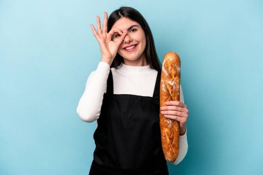 Genç fırıncı Kafkas elinde bir somun ekmekle mavi arka planda izole edilmiş heyecanlı jestler yapıyor..