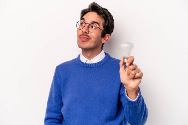 Beyaz arka planda izole edilmiş bir ampul tutan genç beyaz bir adam hedeflerine ve amaçlarına ulaşma hayali kuruyor.