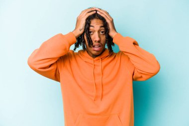 Genç Afrikalı Amerikalı bir adam mavi arka planda izole edilmiş. Şaşırmış ve şok olmuş..