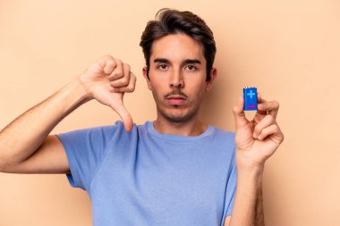 Beyazlı genç bir adam bej arka planda izole edilmiş bir bateriyi tutuyor. Sevilmeyen bir hareket gösteriyor. Anlaşmazlık konsepti.