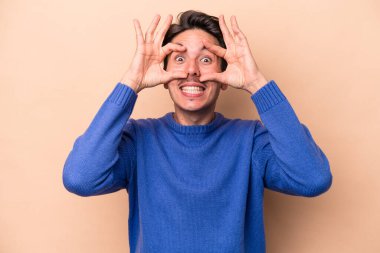 Beyazlı genç bir adam bej arka planda izole edilmiş. Başarı fırsatı bulmak için gözlerini açık tutuyor..