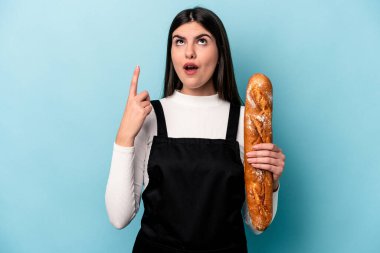 Genç fırıncı Kafkas elinde mavi arka planda izole edilmiş bir somun ekmek açık ağızla üst tarafı işaret ediyor..