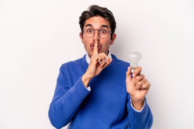 Beyaz arka planda izole edilmiş bir ampul tutan genç beyaz bir adam bir sır saklıyor ya da sessizlik istiyor..
