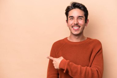 Beyaz tenli genç adam bej arka planda izole edilmiş gülümsüyor ve boş alanda bir şeyler gösteriyor..