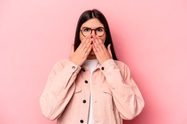 Pembe arka planda izole edilmiş genç beyaz kadın şok olmuş, ağzı ellerle kaplanmış, yeni bir şey keşfetmeye hevesli..