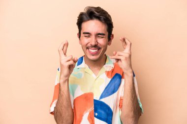 Beyazlı genç adam bej arka planda izole edilmiş şans dilemek için şans diliyor.