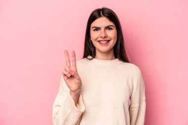Pembe arka planda izole edilmiş genç beyaz kadın zafer işareti gösteriyor ve gülümsüyor..