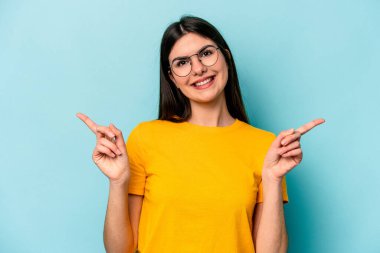 Mavi arka planda izole edilmiş genç beyaz kadın farklı kopya alanlarını gösteriyor, birini seçiyor, parmaklarıyla gösteriyor..