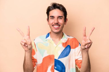 Beyazların arka planında izole edilmiş genç beyaz adam zafer işareti gösteriyor ve gülümsüyor..