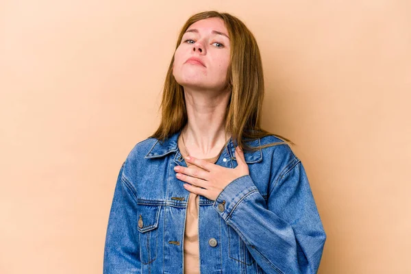 Young English woman isolated on beige background taking an oath, putting hand on chest.