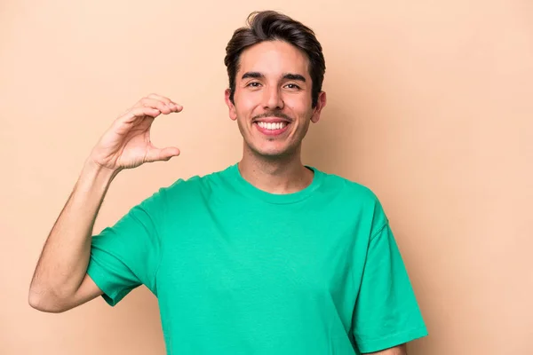 Young Caucasian Man Isolated Beige Background Holding Something Little Forefingers — Stock Photo, Image