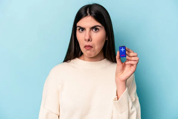 Young Caucasian Woman Holding Batterie Isolated Blue Background Shrugs Shoulders — Stock Photo, Image