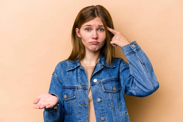 Young English woman isolated on beige background holding and showing a product on hand.