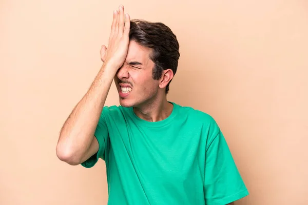 Young caucasian man isolated on beige background forgetting something, slapping forehead with palm and closing eyes.
