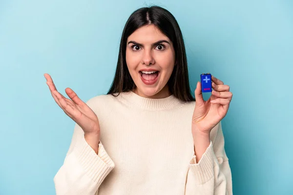 Mladá Běloška Drží Baterii Izolovanou Modrém Pozadí Dostává Příjemné Překvapení — Stock fotografie