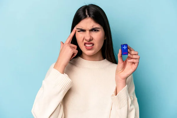 Mladá Běloška Drží Baterii Izolovanou Modrém Pozadí Ukazováčkem Ukazuje Zklamání — Stock fotografie