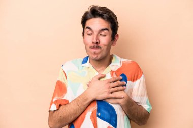 Beyazların arka planında izole edilmiş genç beyaz bir adam dost ifadesine sahip, avuçlarını göğsüne bastırıyor. Aşk konsepti.