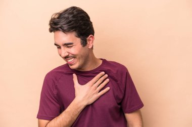 Beyazlı genç bir adam bej arka planda izole edilmiş. Gülüyor, elini kalbe koyuyor, mutluluk kavramını koruyor..