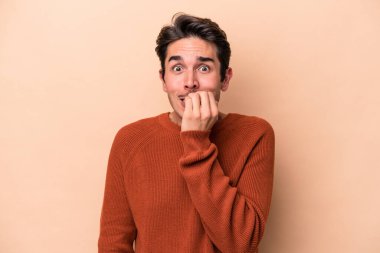 Beyazlı genç bir adam bej arka planda izole edilmiş tırnak yiyor, gergin ve endişeli..