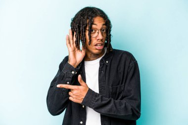 Genç Afrikalı Amerikalı bir adam mavi arka planda izole edilmiş bir şekilde bir dedikoduyu dinlemeye çalışıyor..