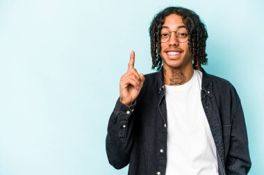 Genç Afrikalı Amerikalı bir adam mavi arka planda izole edilmiş. Bir numarayı parmağıyla gösteriyor..