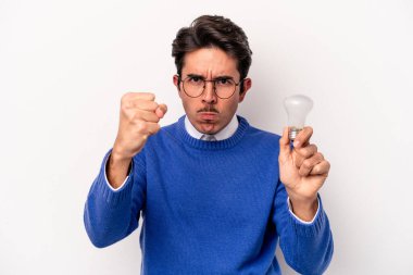 Beyaz arka planda izole edilmiş ampul tutan genç beyaz bir adam kameraya yumruk gösteriyor, agresif bir yüz ifadesi..