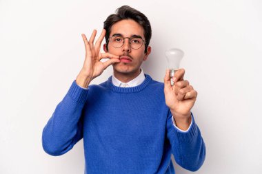 Beyaz arka planda izole edilmiş bir ampul tutan beyaz tenli genç bir adam dudaklarında parmaklarıyla bir sır saklıyor..