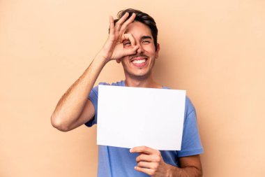 Beyazlı genç bir adam bej arka planda izole edilmiş bir levha tutuyor..