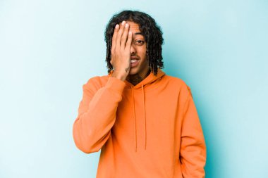 Genç Afrikalı Amerikalı adam mavi arka planda izole edilmiş. Yüzünün yarısını avuç içiyle kaplayarak eğleniyor..