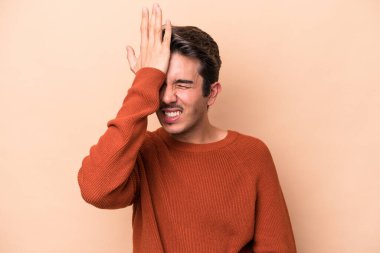 Beyaz tenli genç adam bej arka planda izole edilmiş bir şekilde bir şey unutuyor. Alnına avuç içi ve kapalı gözlerle vuruyor..