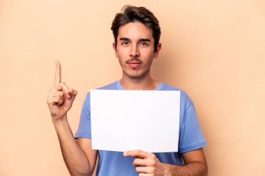 Beyazlı genç bir adam bej arka planda izole edilmiş bir pankart tutuyor. Bir numarayı parmağıyla gösteriyor..