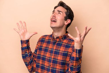 Kafkasyalı genç adam bej arka planda izole edilmiş gökyüzüne haykırıyor, yukarı bakıyor, hayal kırıklığına uğramış.