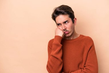 Bej arka planda izole edilmiş, üzgün ve dalgın hisseden, fotokopi alanına bakan genç beyaz bir adam..