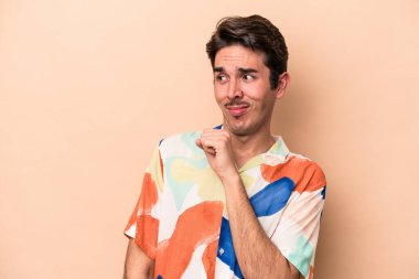 Kafkasyalı genç adam bej arka planda izole, kafası karışmış, şüpheli ve güvensiz hissediyor..