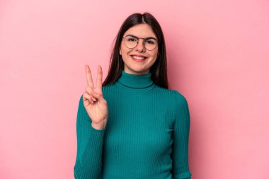Pembe arka planda izole edilmiş genç beyaz kadın iki numarayı parmaklarıyla gösteriyor..