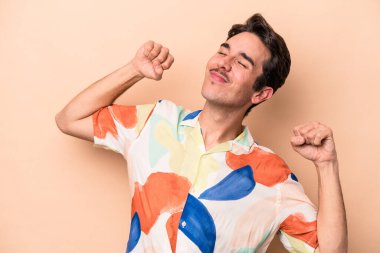 Beyazlı genç bir adam bej arka planda izole edilmiş, kollarını uzatmış, rahat bir konumda..