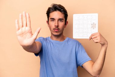 Elinde bej arka planda izole edilmiş bir yapboz tutan genç beyaz bir adam elini uzatmış, dur işareti göstererek seni engelliyor..