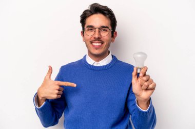 Beyaz arka plandaki ampulü tutan beyaz tenli genç adam gömlek fotokopi alanını işaret ediyor, gururlu ve kendinden emin.