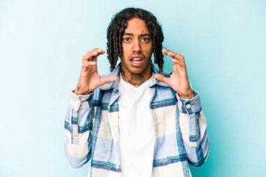 Genç Afrikalı Amerikalı adam mavi arka planda izole edilmiş gergin elleriyle çığlık atıyor..