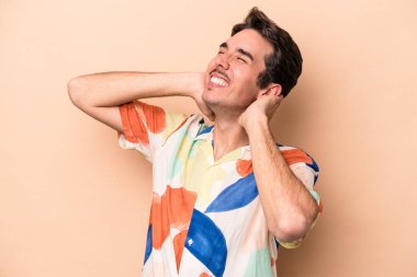 Beyazlı genç bir adam bej arka planda izole edilmiş. Kendine güveniyor, elleri başının arkasında..