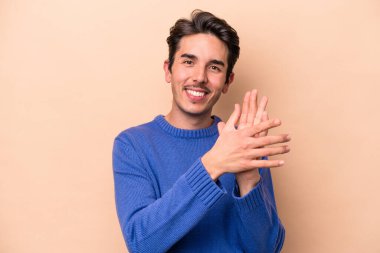 Beyaz tenli genç adam bej arka planda izole edilmiş enerjik ve rahat hissediyor, ellerini ovuşturuyor kendinden emin..