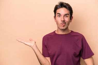 Beyaz, bej arka planda izole edilmiş genç bir adam bir avuç içinde fotokopi alanı ve belinde bir el daha gösteriyor..