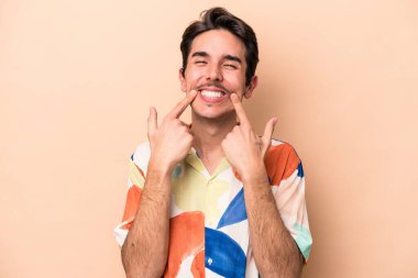 Beyazların arka planında izole edilmiş genç beyaz adam gülümsüyor, parmaklarını ağzına doğrultuyor..