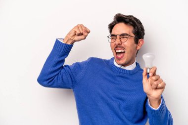 Beyaz arka planda izole edilmiş bir ampul tutan genç beyaz adam zaferden sonra yumruğunu kaldırıyor, kazanan konsept.