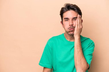 Bej arka planda izole edilmiş, üzgün ve dalgın hisseden, fotokopi alanına bakan genç beyaz bir adam..