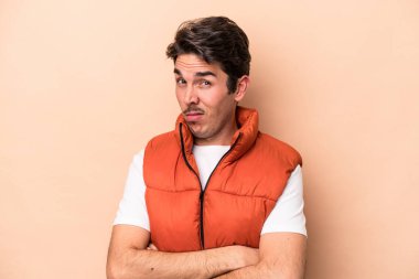 Beyazlı genç adam bej arka planda izole edilmiş. Mutsuz, iğneleyici bir ifadeyle kameraya bakıyor..