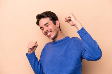 Beyazlı genç adam bej arka planda izole edilmiş özel bir günü kutluyor, atlıyor ve enerjiyle kollarını kaldırıyor..