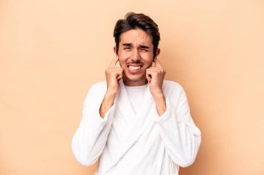 Bornoz giyen beyaz bir genç adam bej arka planda izole edilmiş kulakları elleriyle kapatıyor..