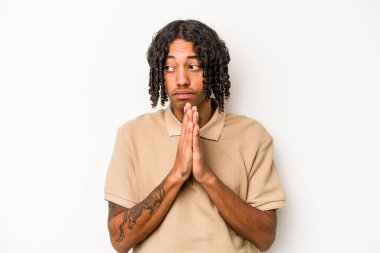 Genç Afrikalı Amerikalı adam beyaz arka planda izole edilmiş dua ediyor, bağlılık gösteriyor, dindar biri ilahi ilham arıyor..
