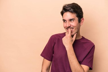 Beyaz tenli genç adam bej arka planda izole edilmiş. Rahatlamış bir şekilde fotokopi odasına bakan bir şey düşünüyor..